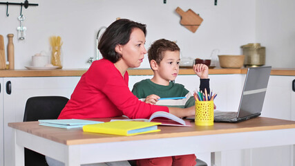Female private tutor helping young student with homework at desk in bright child's room. mother...
