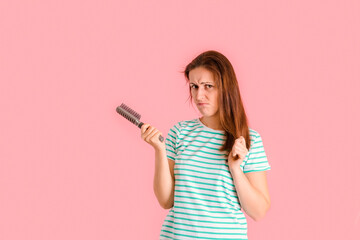 Naklejka premium A middle-aged girl combs her hair and frowns because of split ends of her hair, pink background
