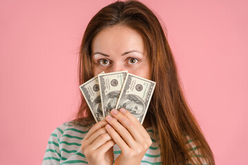 A beautiful brunette woman in casual clothes won a small amount of money in a lottery. Portrait of a girl with dollar bills covering her face