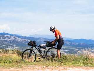 Fototapeta na wymiar Cyclist man traveling with a bicycle in nature sorts his backpack. Bikepacker