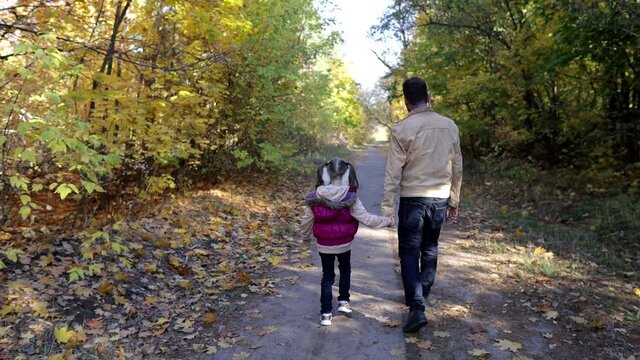 a man walks with a little girl in the autumn park, father and daughter play together