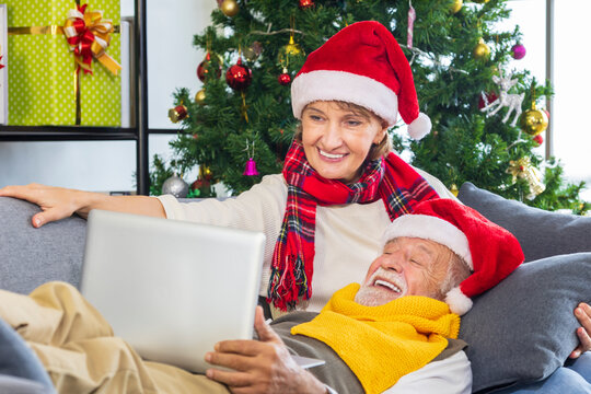 Senior caucasian couple celebrating Christmas together in happiness while having video call to the family at home using laptop computer while wearing red Santa hat in decorated Christmas tree