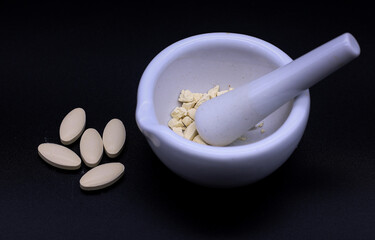 The tablets were crushed in a mortar. There were several pills on the side.  photographed on a black background.