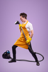 Housekeeper having fun with vacuum cleaner on violet background