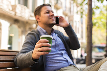 Man walking on the street, drinking coffee, talking by phone