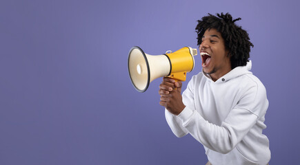 Emotional black teen guy shouting into megaphone, announcing breaking news over violet background
