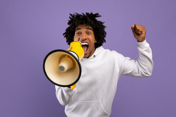 Agitated black teenager shouting into megaphone over violet studio background - obrazy, fototapety, plakaty