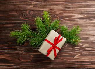 Gift box in craft paper and a red bow on fir branches on a wooden background.