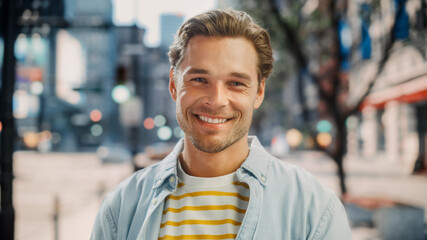 Fototapeta premium Portrait of a Happy Handsome Young Man in Casual Clothes Posing on the Street. Successful Male Model in Big City Living the Urban Lifestyle. Background with Office Buildings and Billboards.