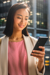Portrait of an Attractive Japanese Female Wearing Smart Casual Clothes and Using Smartphone on the Urban Street. Manager in Big City Connecting with People Online, Messaging and Browsing Internet.