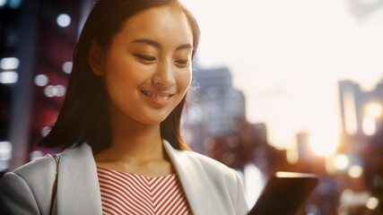 Close Up Portrait of an Attractive Japanese Female Wearing Smart Casual Clothes and Using Smartphone in a City at Sunset. Stylish Woman Connecting with People Online, Messaging and Browsing Internet.