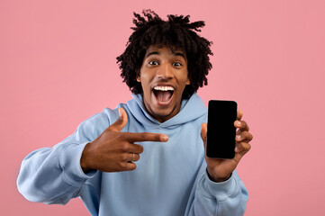Excited black teenager pointing at cellphone with blank screen on pink background, space for mobile app or website