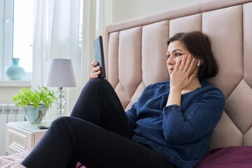 Sad middle aged woman in headphones looking into the smartphone screen.