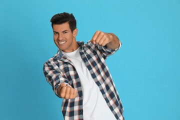 Happy man pretending to drive car on light blue background