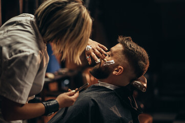 Man getting shaved with straight edge razor by hairdresser at barbershop