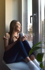 the girl sits on the windowsill and drinks coffee