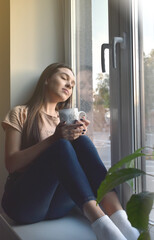 the girl sits on the windowsill and drinks coffee