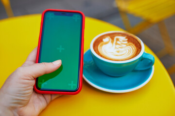 Cup of fresh flat white coffee with milk drawing and smartphone with mockup green screen