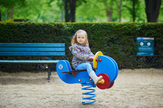 Adorable toddler girl having fun on spring rider on playground on a fall day