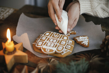 Decorating christmas gingerbread cookies with icing on wooden table with candle and ornaments....