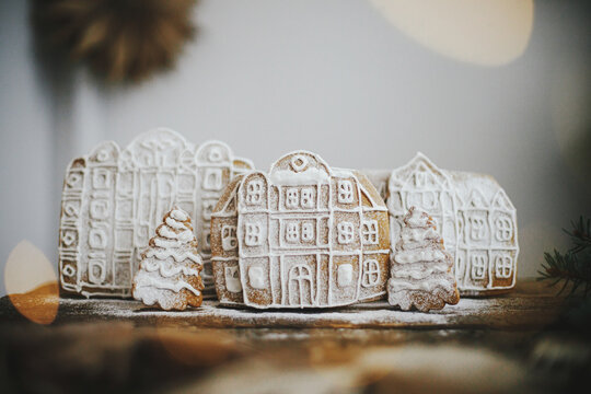 Merry Christmas and Happy Holidays! Christmas gingerbread houses and trees in snow on rustic wood with golden lights. Atmospheric moody image. Christmas cookies village scene. Season greeting