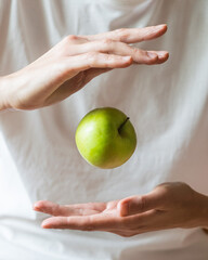 Whole green apple levitates above the hands in the air on a white background, selective focus....
