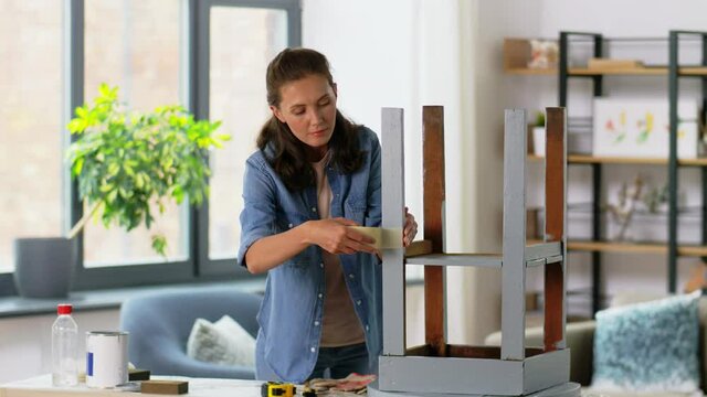 repair, diy and home improvement concept - happy smiling woman sticking adhesive tape to old wooden table for repainting it