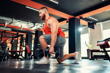 Fototapeta na wymiar A young bearded athletic man trains with dumbbells in the gym. Squat exercise. Bottom view. The concept of fitness and workout