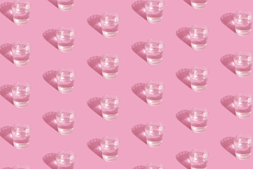 Glasses with water and shadow pattern on pink background