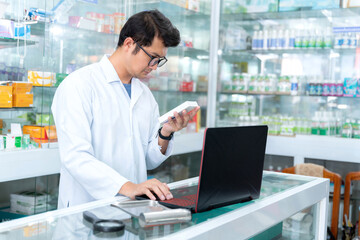 Portrait of young male pharmacist holding medication while using laptop at pharmacy counter