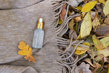 cosmetic oil for face in a jar with a dropper on scarf and autumn leaves background