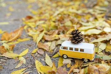 classic yellow bus toy with pine cone on road with yellow falling leaves, autumn seasonal background. symbol of fall time. vacation adventure and travel concept