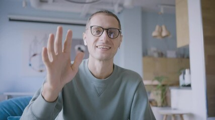 Positive man psychotherapist with glasses waves hand beginning online consultation with client at videochat in clinic office camera close view
