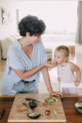 Naklejka premium Lovely cute Caucasian family making healthy food at kitchen. Portrait of smiling mother and children making salad. Happy family activity together
