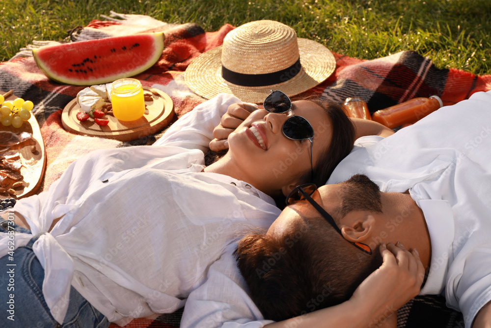 Poster Happy young couple resting on picnic plaid outdoors