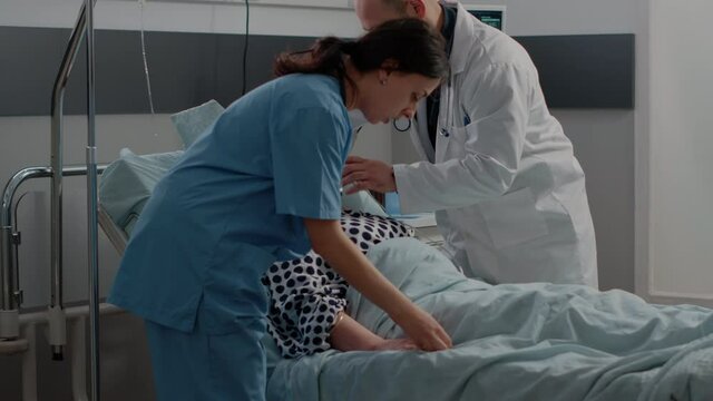 Ill woman with heavy breathing asking for medical help in bed while doctor and nurse rushing to give assistance for healthcare. Specialists helping old patient with respiratory problem