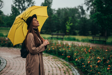 Woman holding a yellow umbrella and enjoying a walk in the park during rain