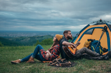 Couple of campers spending time together in the nature while playing guitar