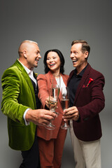 Cheerful interracial friends holding glasses of champagne isolated on grey