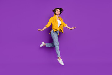 Photo of funny sweet young lady wear yellow shirt jumping high smiling isolated violet color background