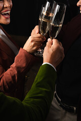 Cropped view of excited asian woman toasting champagne with friends isolated on black on black background
