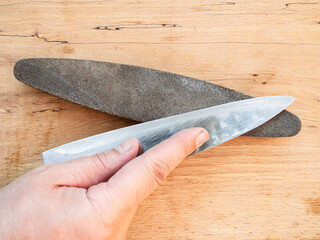 hand sharpens kitchen knife closeup on whetstone