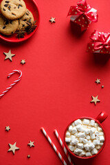Christmas or New Year red background with mug of hot chocolate with marshmallows, oatmeal cookies, candy canes, Christmas decorations. Flat lay, top view, overhead.