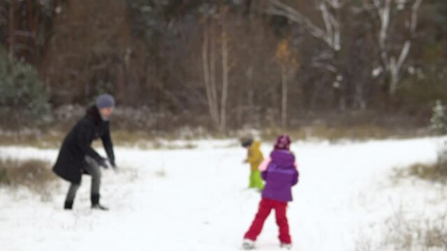 Blurred image of a family of four: mom, dad, son and daughter are playing snowballs in nature.