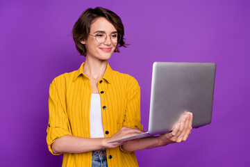 Portrait of attractive cheery focused girl using laptop e commerce chat isolated over bright violet...