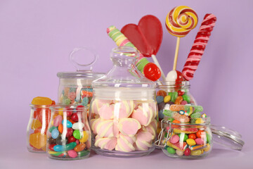 Fototapeta na wymiar Jars with different delicious candies on violet background
