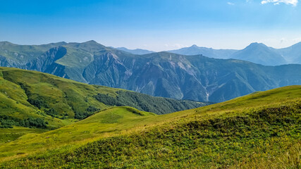 A panoramic view on high Caucasus mountains in Georgia. There are high, snowcapped peaks in the back. Lush pasture in front. Idyllic landscape. Calmness and meditation. Natural remedy