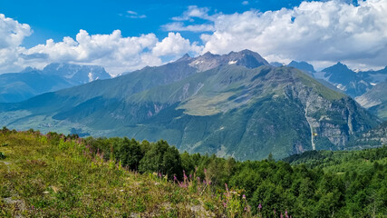A panoramic view on high Caucasus mountains in Georgia. There are high glaciers in the back. Thick clouds above the sharp peaks. Lush pastures on the sides. Barren peaks. Idyllic landscape.