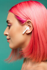 profile of young woman with pink dyed hair in wireless earphone isolated on blue