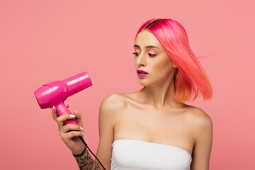 tattooed young woman with colorful hair using hair dryer isolated on pink